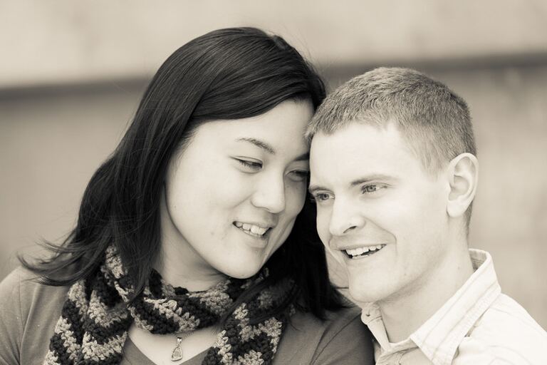 Sepia-toned portrait of a young couple cheek to cheek, the woman in a crocheted scarf and the short-haired man both smiling.